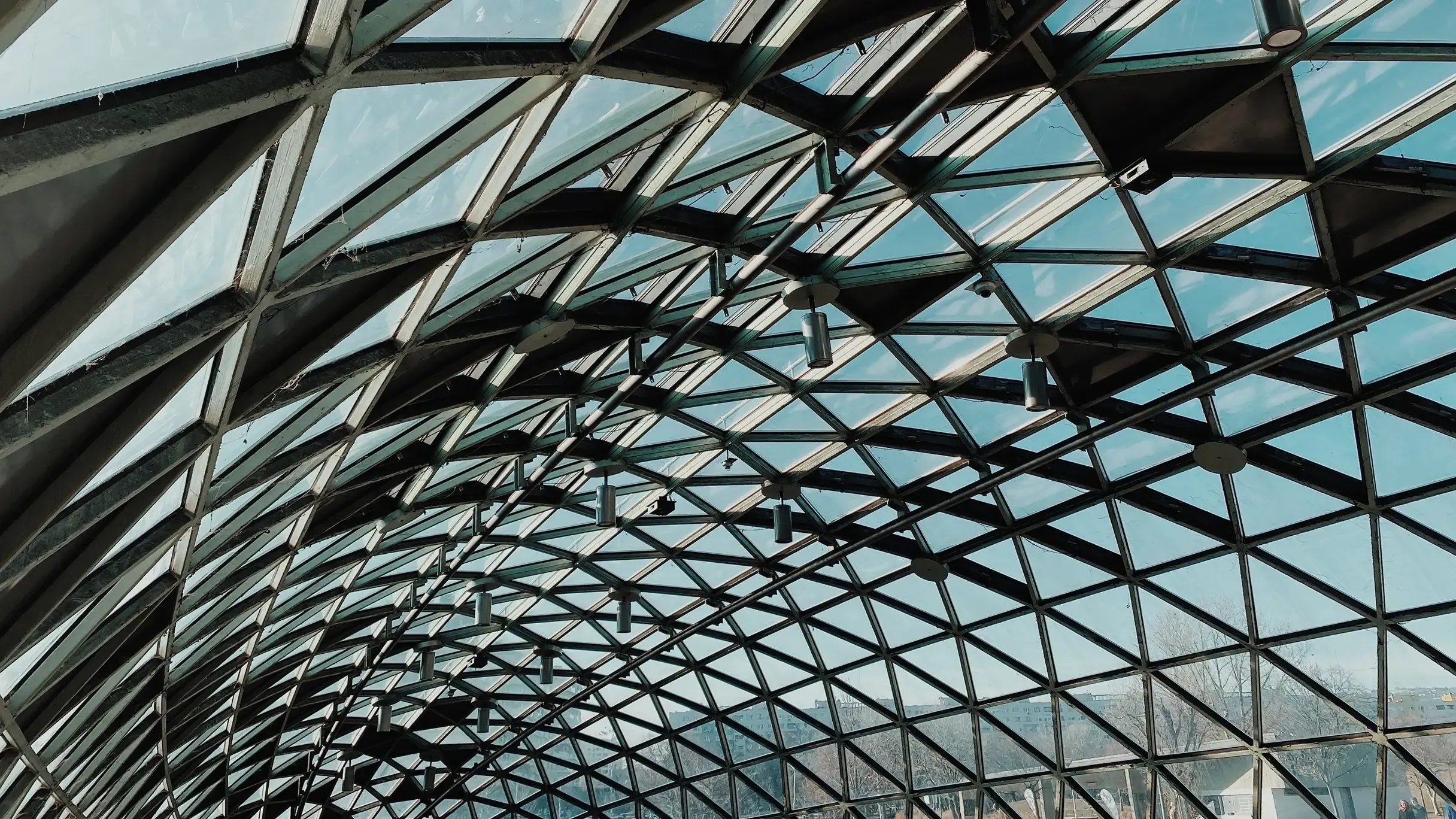 Low-angle view of an intricate, curved glass gridshell roof. 
