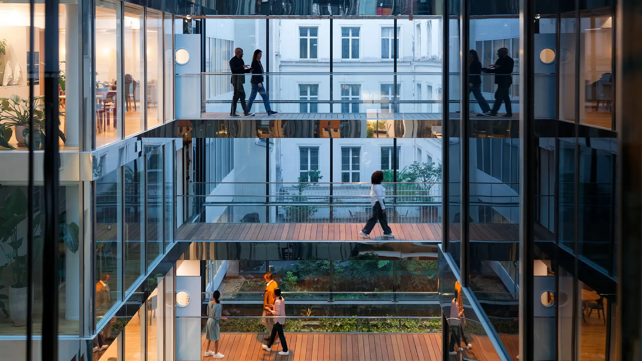 People walk between offices, their reflections showing in polished surfaces.