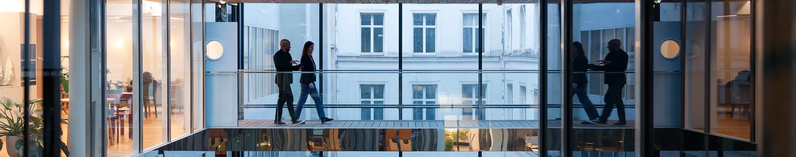 People walk between offices, their reflections showing in polished surfaces.